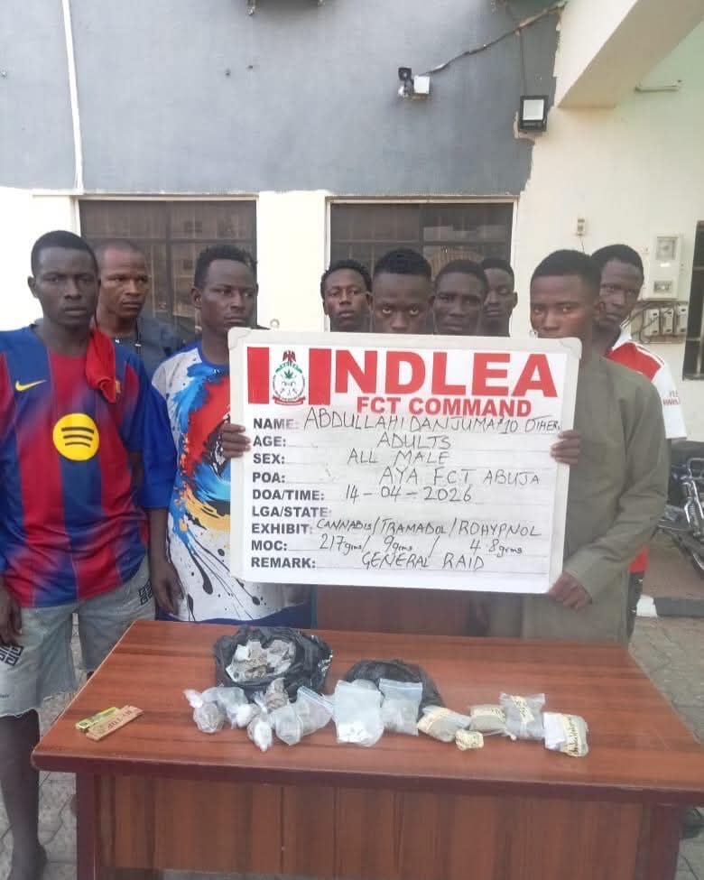 Group of young men standing behind a sign that reads IN DLEA FCT COMMAND while drugs are displayed on a table in front of them.