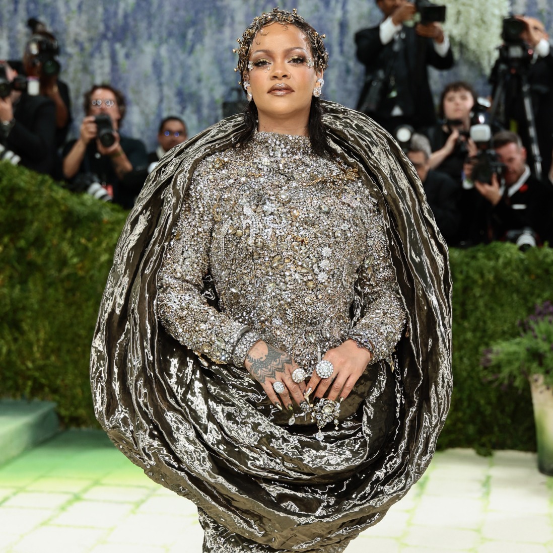 Rihanna (Marie Claire) - THEWILL NEWS MEDIA Rihanna wearing a bejeweled silver gown with a dramatic cape at a red-carpet event, photographers in the background.