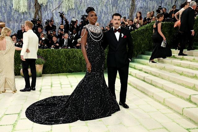 Venus Williams (Aol.com) - THEWILL NEWS MEDIA A glamorous couple poses on a light stone staircase at a red-carpet event; woman in a black sequin gown with a pearl statement necklace, man in a tuxedo.