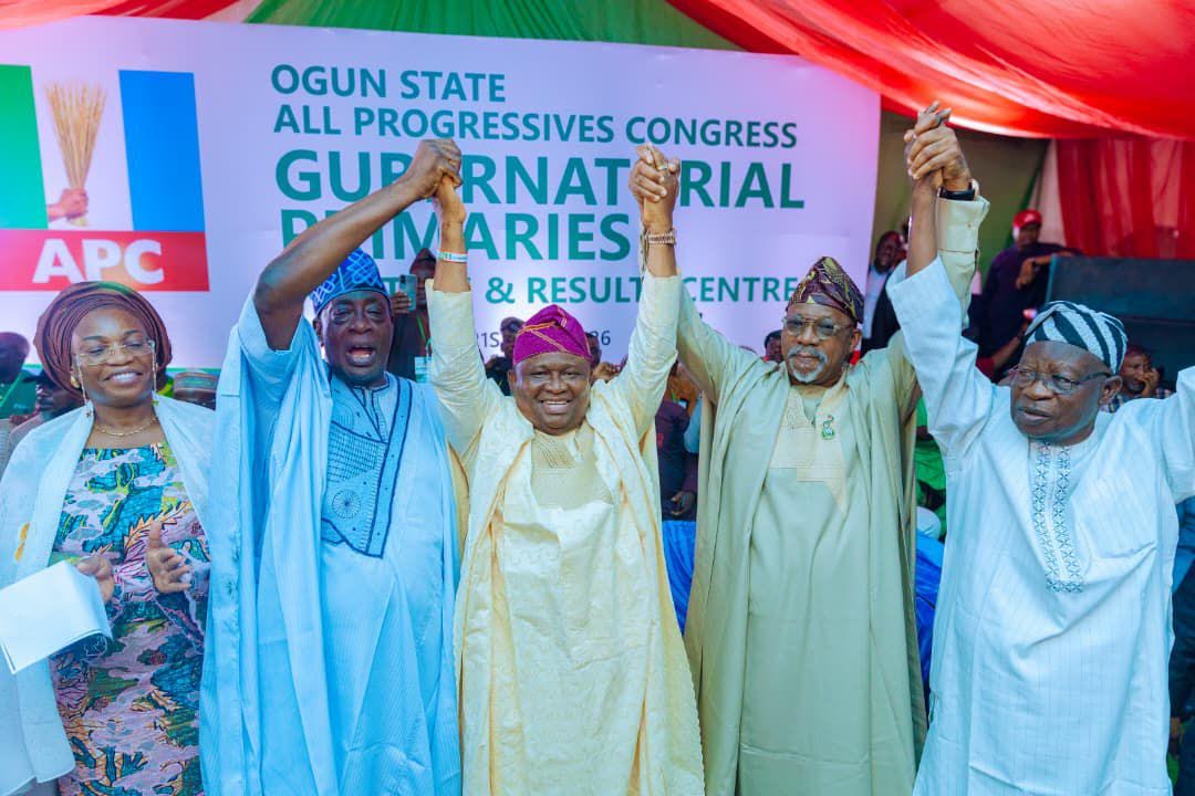 Ogun-APC-governorship-candidate-Senator-Solomon-Olamilekan-Adeola-being-officially-presented-at-the-party-secretariat-after-his-emergence - THEWILL NEWS MEDIA Five people on a stage raise their clasped hands in celebration at a political rally with an APC banner in the background.