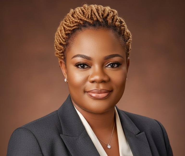 DTF 2026 - THEWILL NEWS MEDIA Professional headshot: woman in a dark blazer with neutral makeup, short twisted hair, against a brown backdrop.