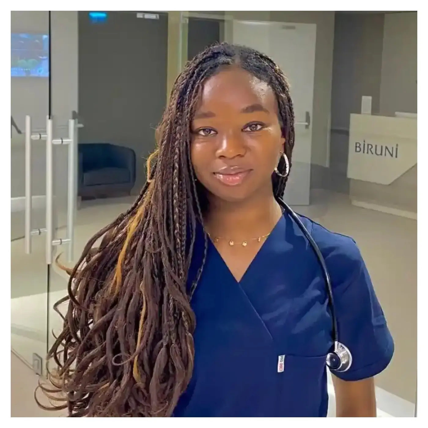 23-year-old-Nigerian-medical-doctor-Adaobi-Nnani - THEWILL NEWS MEDIA Portrait of a healthcare professional with long braided hair, wearing navy scrubs and a stethoscope, standing in a modern clinic lobby.