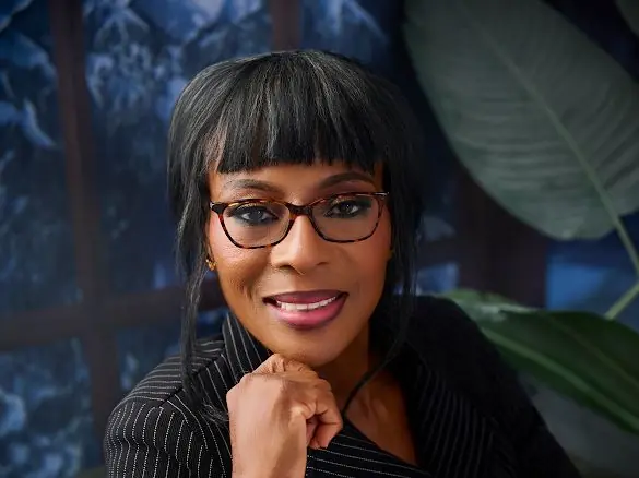 Portrait of a smiling woman with short black hair and glasses, resting her chin on her hand in a professional setting.