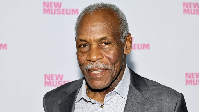 Portrait of an older Black man in a gray suit at a New Museum event backdrop with pink logos in the background