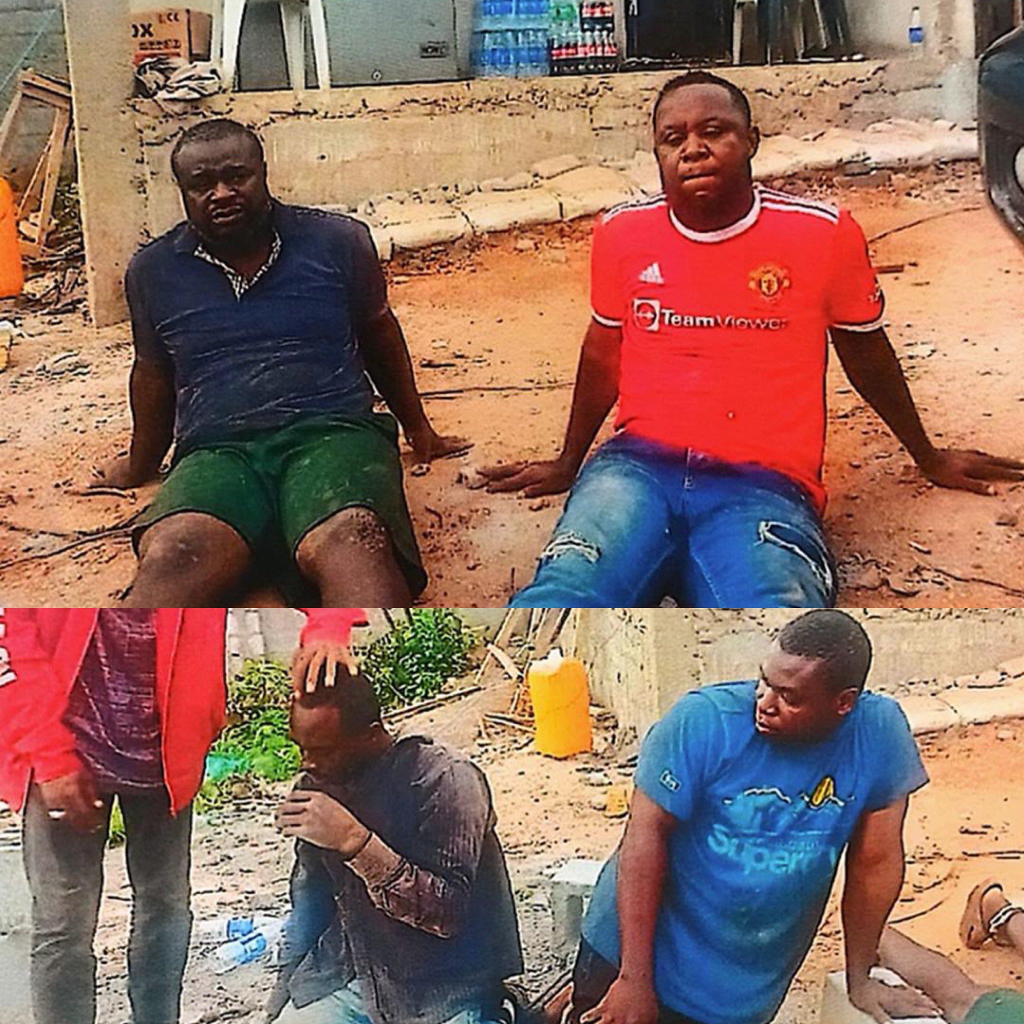 Three men sit on a dusty, construction-like ground in front of a shop, one in a red Manchester United jersey and the others in dark/blue shirts.