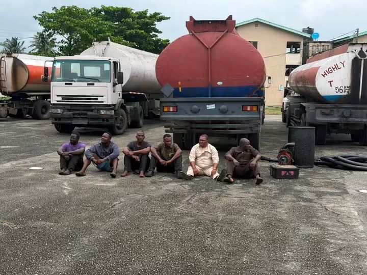Six suspects arrested by troops of the Nigerian Army's 65 Battalion sit beside tanker trucks and equipment recovered during an intelligence-led raid on a suspected illegal bunkering site in the Orile General Area of Lagos State on Tuesday. Photo credit: Nigerian Army. - THEWILL NEWS MEDIA