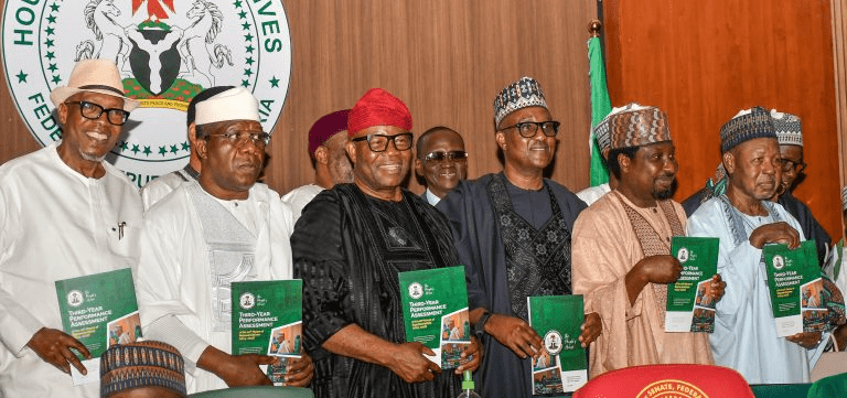 Group of Nigerian officials in traditional and formal attire, each holding a green report booklet at a formal event in front of a government seal backdrop.