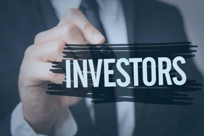 Hand overlaying the word INVESTORS on a dark glass panel with brush-stroke accents, suggesting finance or investment topics.