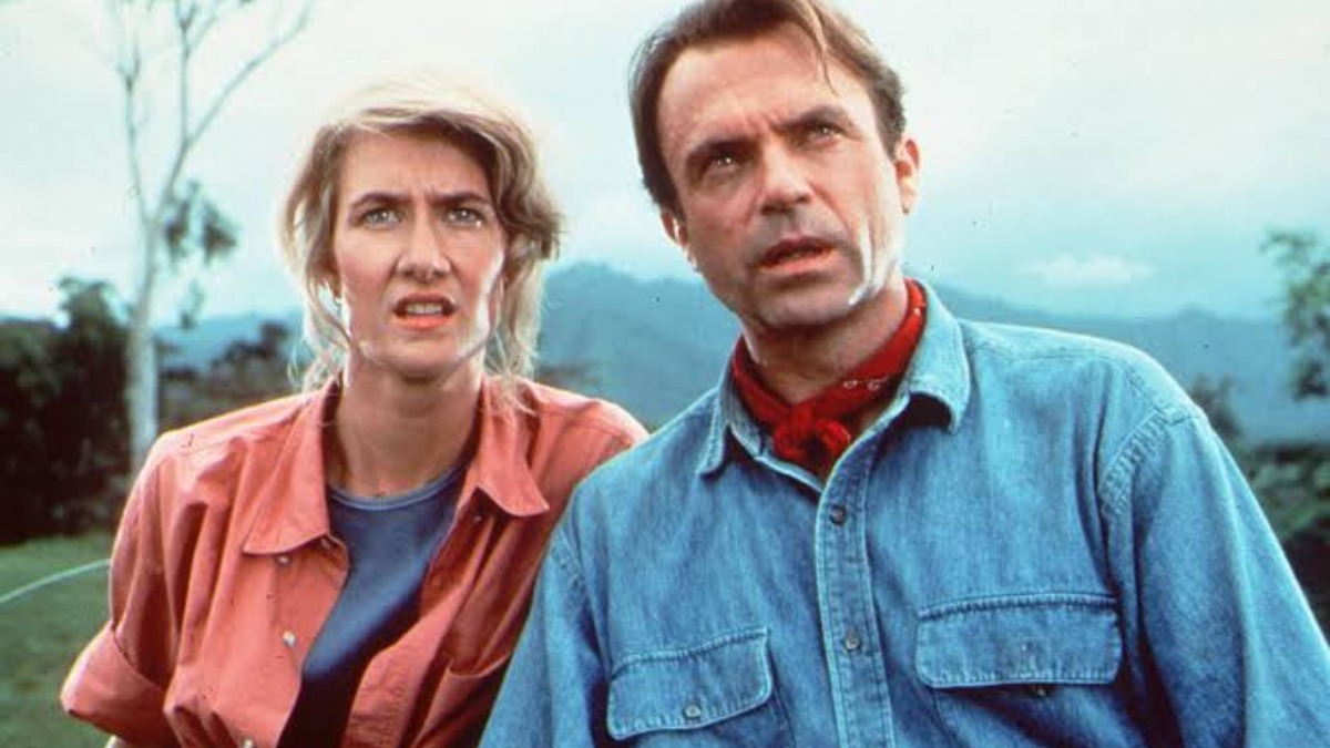 Two adults outdoors with surprised expressions, standing in a grassy, hilly landscape.