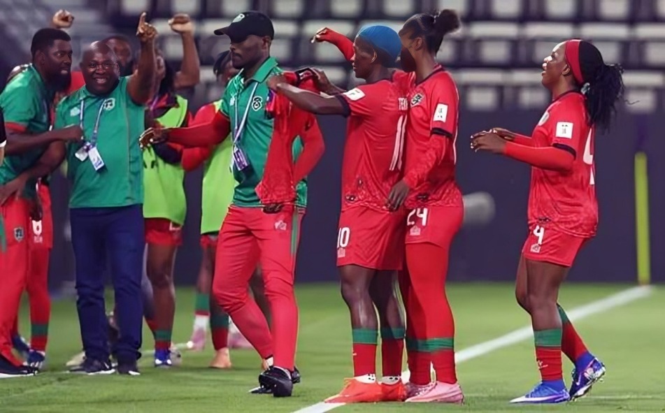 Malawi women's national team - THEWILL NEWS MEDIA Soccer players in red and green celebrate on the field, raising arms in victory with medals visible on some players.
