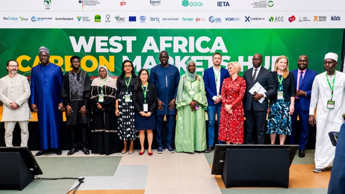 A representation of harmonised regional framework - THEWILL NEWS MEDIA Diverse professionals posing for a photo in front of a green West Africa Carbon Markets Hub banner at a conference event in Africa.