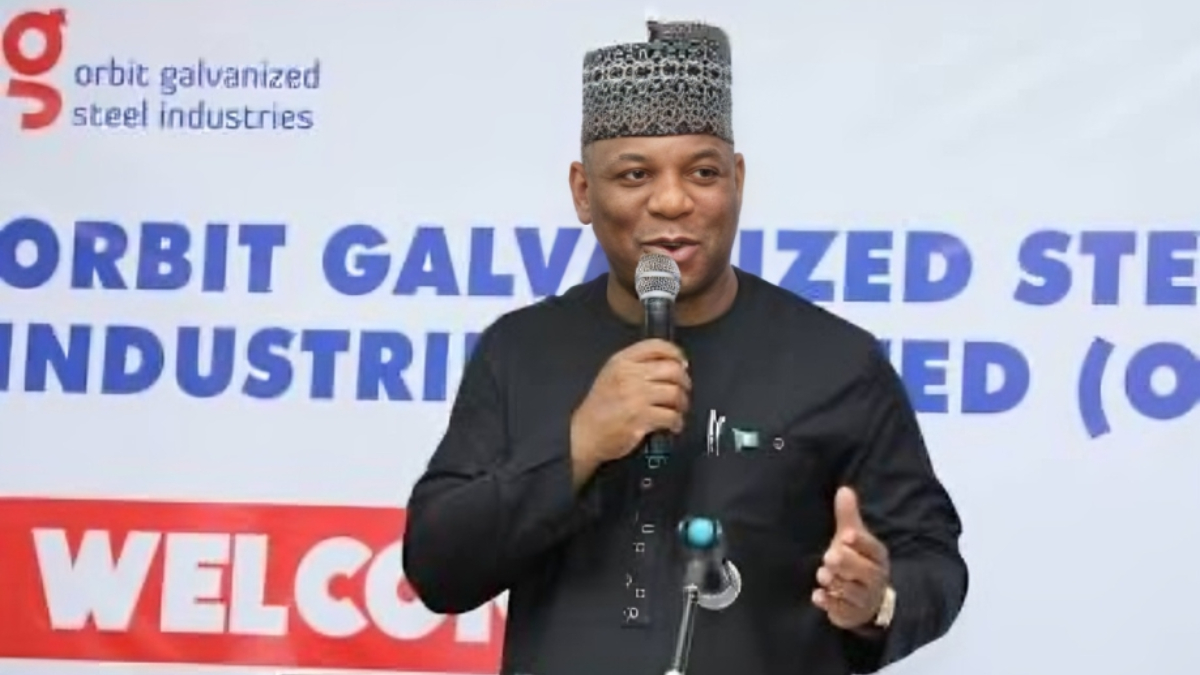 Abubakar Audu - THEWILL NEWS MEDIA Man in traditional attire speaks into a microphone at a welcome event with a banner for Orbit Galvanized Steel Industries in the background.