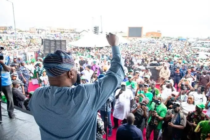 Atiku at osun 1 - THEWILL NEWS MEDIA Man on stage raises his fist toward a dense outdoor crowd at a rally or concert.