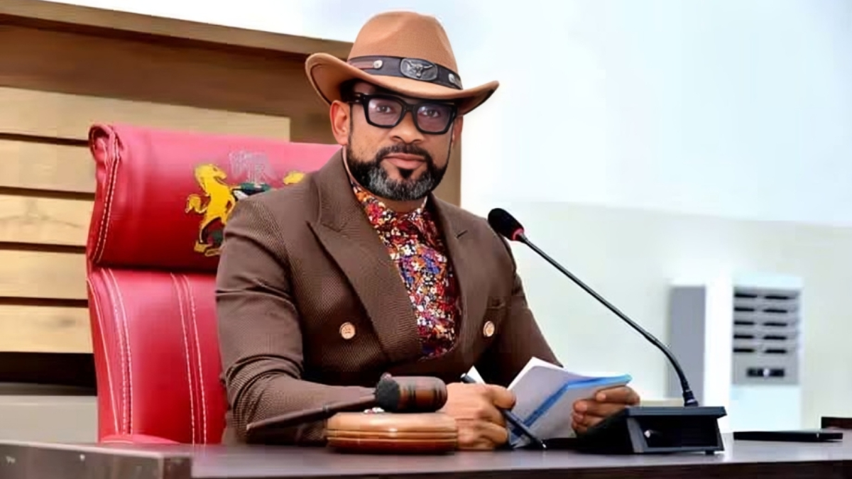 Blessing Agbebaku - THEWILL NEWS MEDIA Man in a brown suit and hat sits at a judge’s desk with a microphone, gavel, and papers ahead of him.