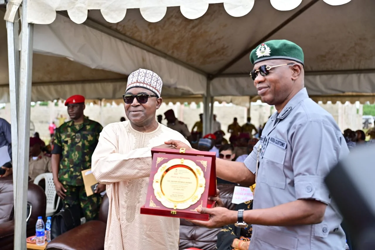Buba Marwa and Bashir Adewale Adeniyi - THEWILL NEWS MEDIA Man in beige traditional attire receives a decorative plaque from a uniformed officer under a canopy at an outdoor ceremony.