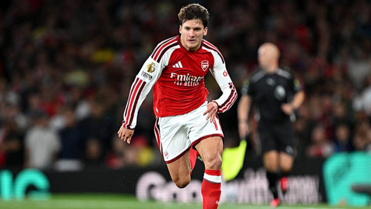Christos Tzolis - THEWILL NEWS MEDIA Arsenal footballer in red and white kit sprinting on a pitch during a match, with a referee in the blurred background edge of the scene.