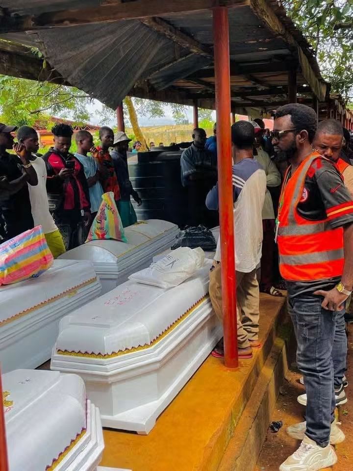 Coffins of victims of violence - THEWILL NEWS MEDIA Caskets lined up under a simple shelter as mourners gather at an outdoor funeral ceremony, with a man in an orange vest among them.