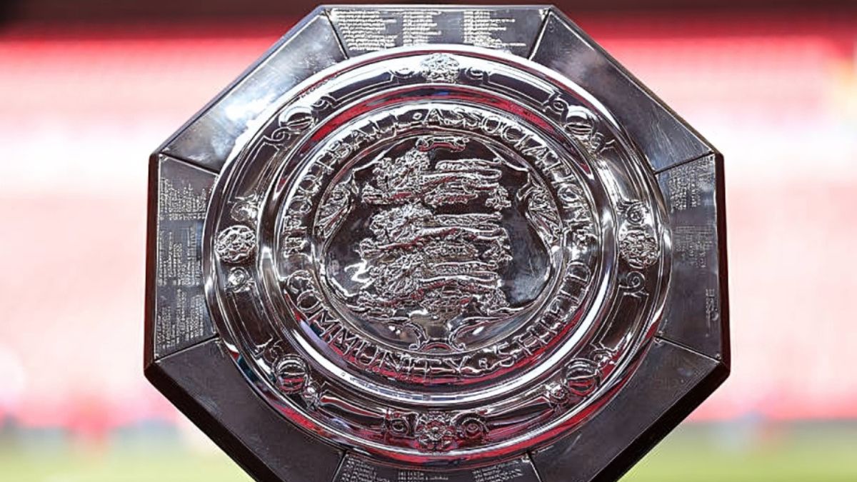 FA Community shield trophy - THEWILL NEWS MEDIA Shiny silver octagonal trophy with intricate engravings, set against a blurred stadium background.