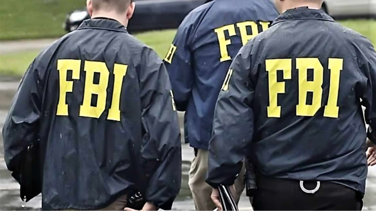 FBI - THEWILL NEWS MEDIA Back view of three FBI agents wearing dark jackets with bold yellow 'FBI' letters, walking away in an outdoor setting.