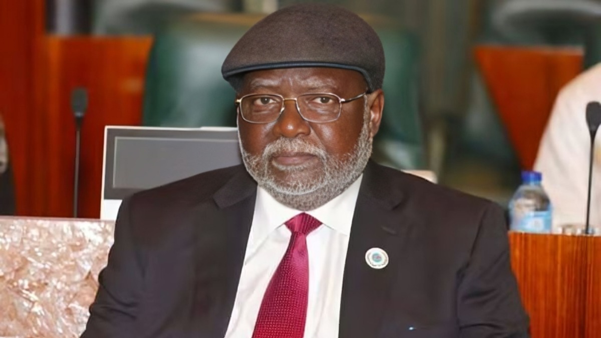 Former Chief Justice of Nigeria Justice Olukayode Ariwola - THEWILL NEWS MEDIA Older man in a black suit and red tie wearing glasses and a dark beret, seated at a conference table with a pin on his lapel.