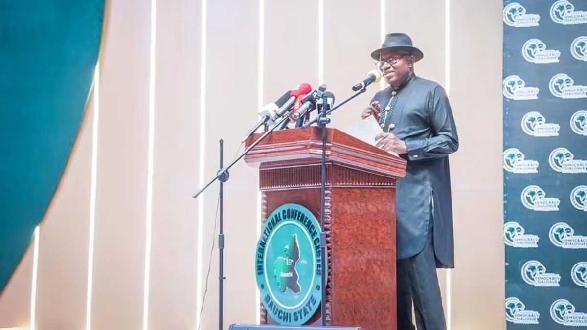 Former President Goodluck Ebele Jonathan - THEWILL NEWS MEDIA An African man in a dark suit and hat speaks from a wooden podium with multiple microphones during a conference.