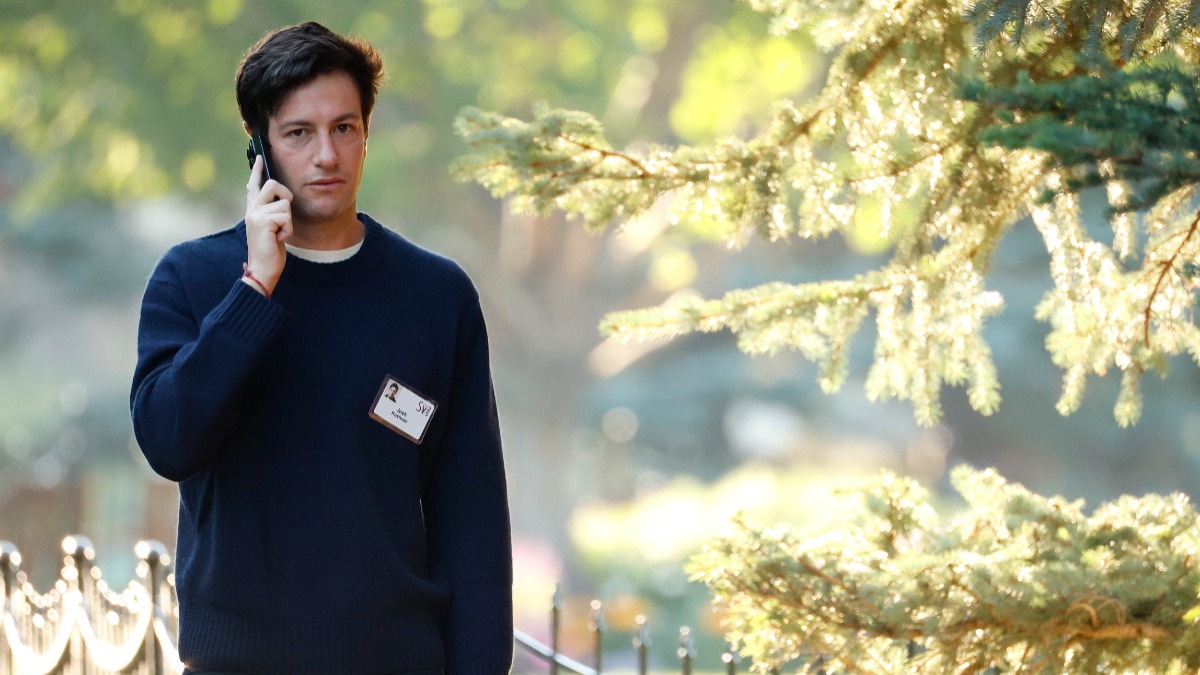 Man in a navy sweater talks on a cell phone outdoors, wearing an ID badge on his chest.