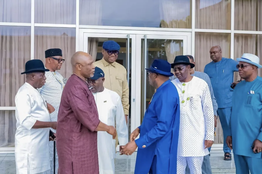 Fubara Hosts Magnus Abe-Led Rainbow Coalition Committee 2 - THEWILL NEWS MEDIA Group of men in colorful traditional attire outside a glass-front building, with two men shaking hands as others watch.