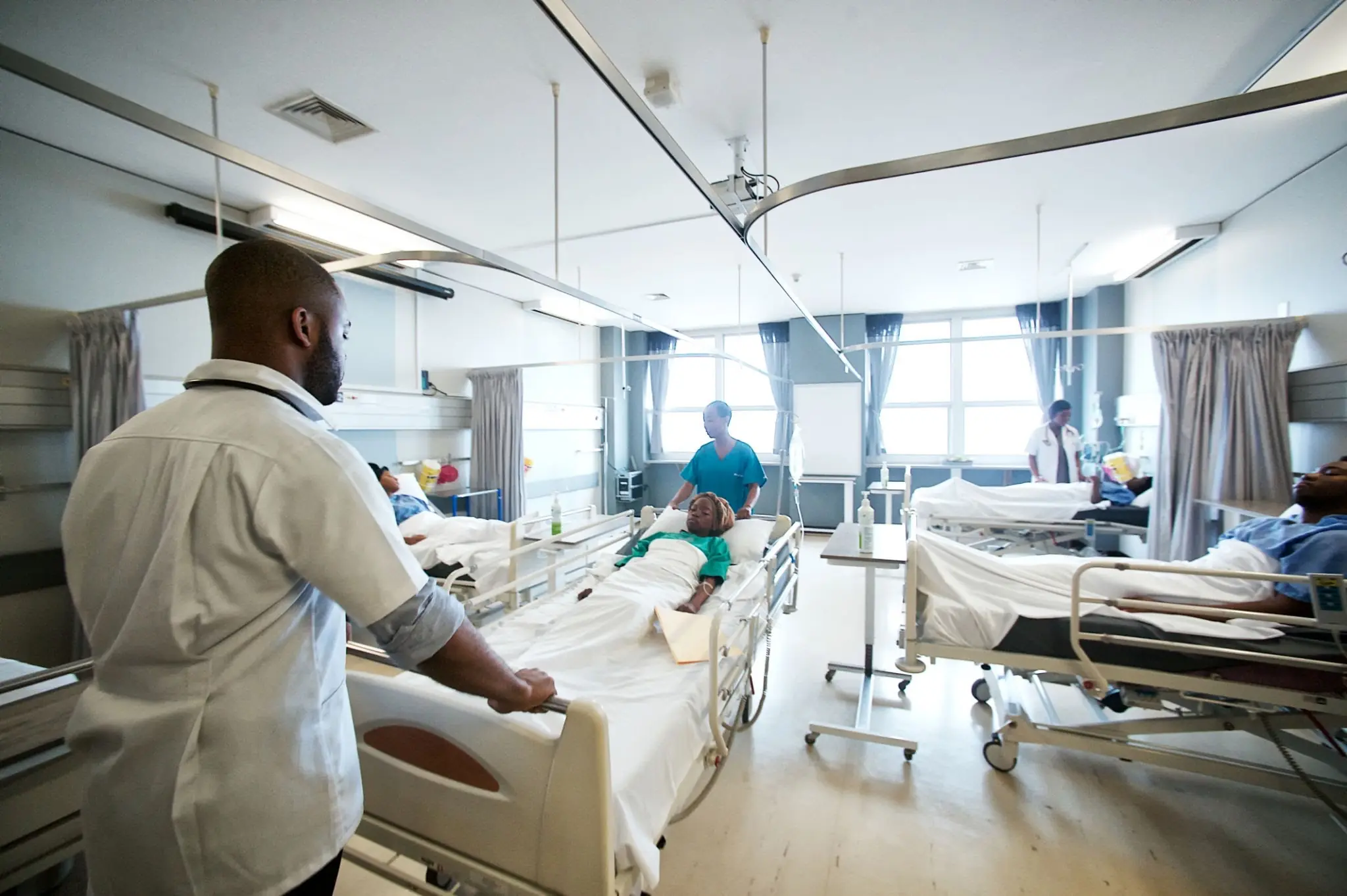 Hospital ward and clinical care area - THEWILL NEWS MEDIA Healthcare workers attend to patients in a bright hospital ward with multiple beds and curtains
