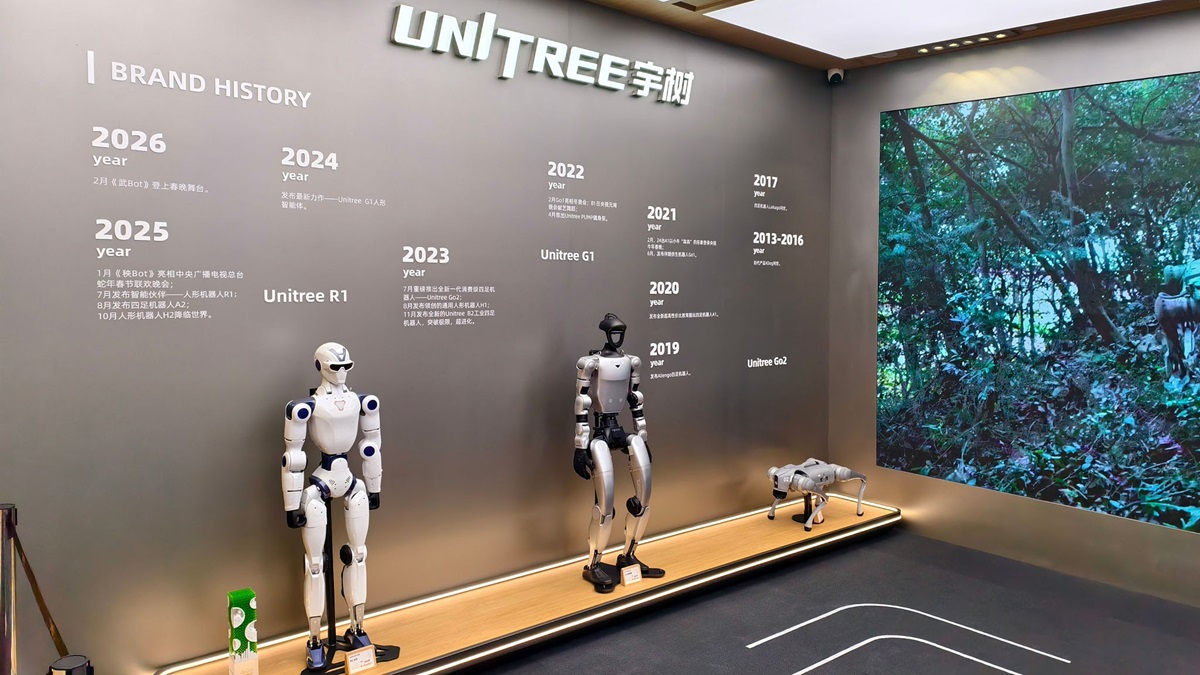 Humanoid Robot - THEWILL NEWS MEDIA Unitree brand history exhibit: wall timeline with years and two humanoid robots, plus a large forest video screen.