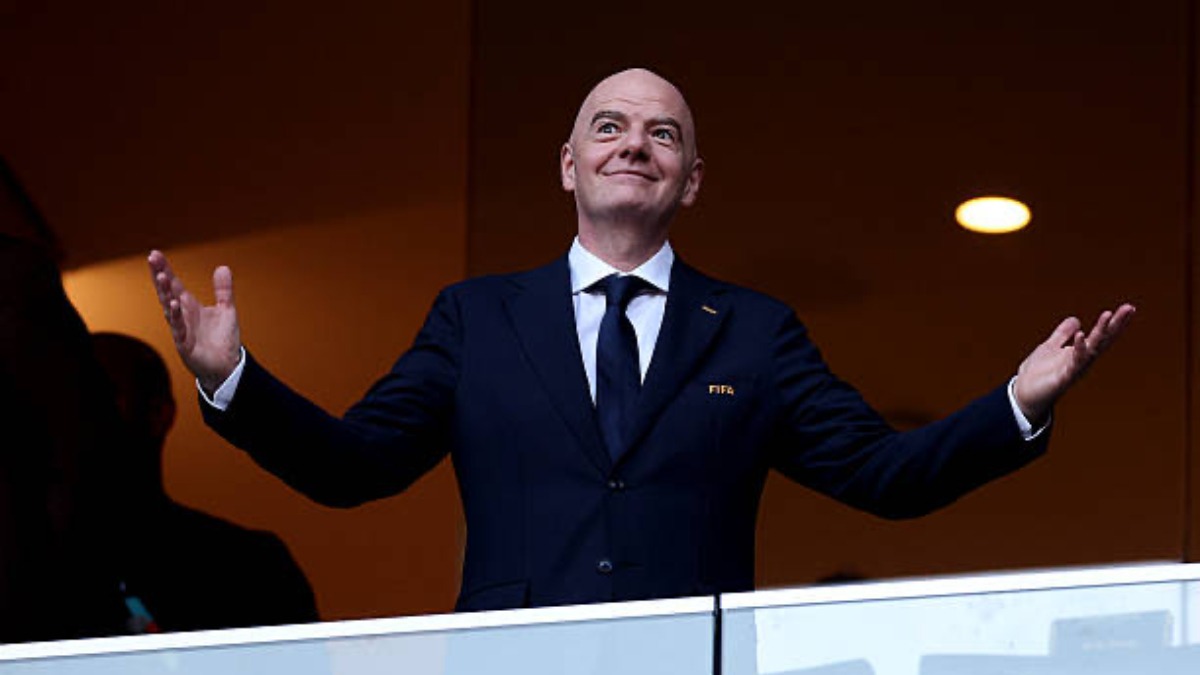 Infantino - THEWILL NEWS MEDIA Man in a navy suit with arms outstretched on a stage, smiling at an audience.