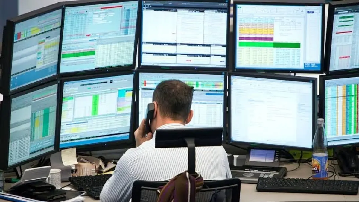 Institutional Market Analytics Trading Terminal - THEWILL NEWS MEDIA Trader at a multi-monitor trading desk, reviewing financial dashboards while on a phone call.