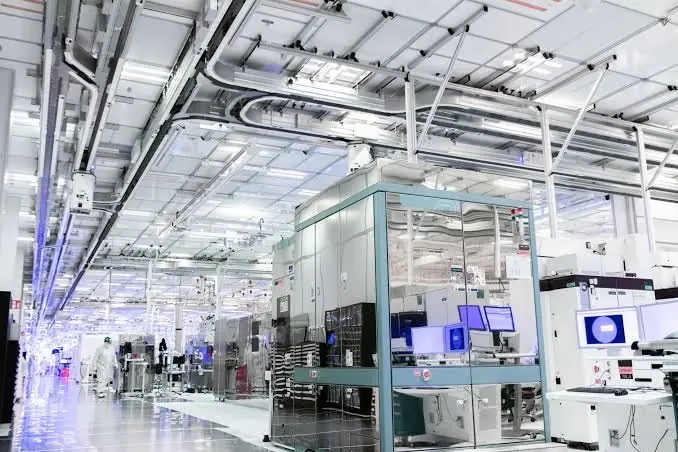 Intel advanced semiconductor fab cleanroom facility - THEWILL NEWS MEDIA Inside a modern electronics manufacturing cleanroom with robotic equipment and workers in white coats.