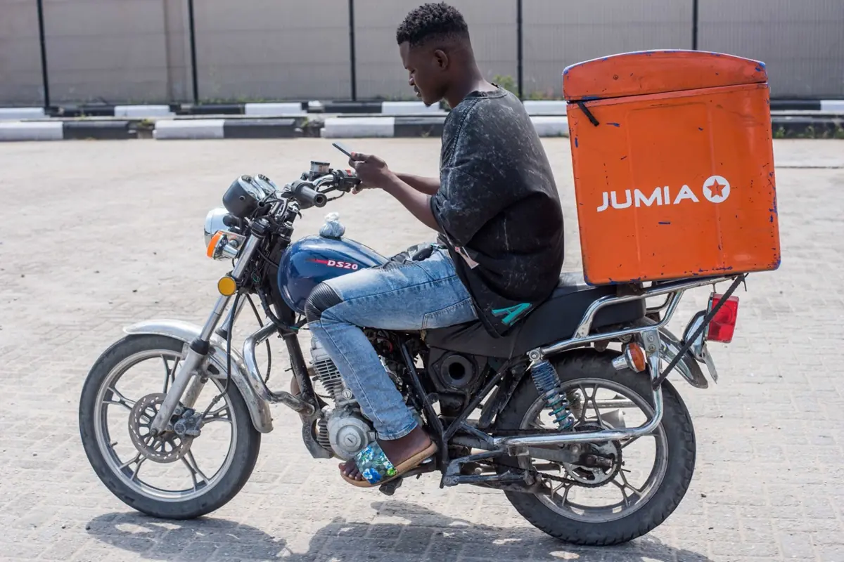 JUMIA - THEWILL NEWS MEDIA Delivery rider on a blue motorcycle with an orange Jumia delivery box mounted at the rear.