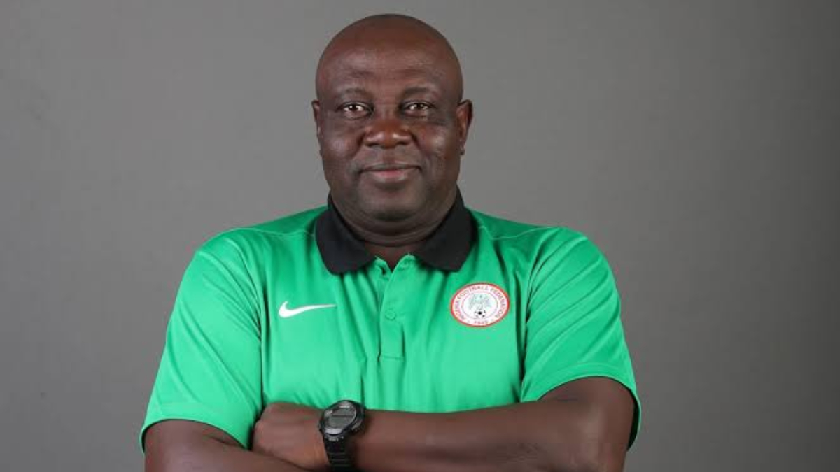 Justin Madugu - THEWILL NEWS MEDIA Portrait of a dark-skinned man in a green polo shirt with a circular crest on the left chest, arms crossed, wearing a black watch, in a gray studio backdrop.