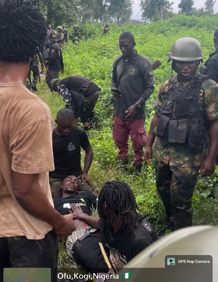 Kogi Kidnap Victims 3 - THEWILL NEWS MEDIA Group of armed men in a grassy field; one man lies on the ground while another kneels beside him with a hand on his chest.
