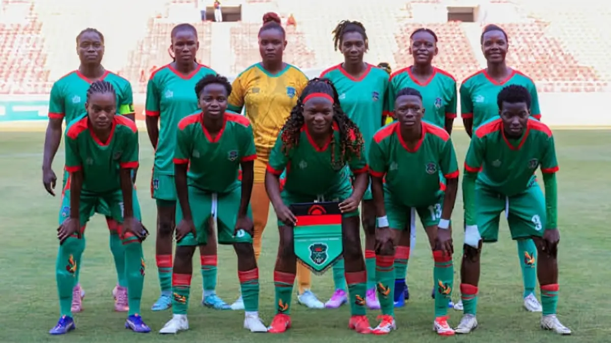 Malawi girls - THEWILL NEWS MEDIA Women’s soccer team in green and red jerseys pose for a group photo on a grassy field, with a yellow-clad goalkeeper in the back row.