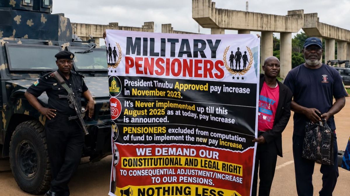 Group of men posing with a large banner reading'MILITARY PENSIONERS' during a protest near military vehicles and concrete structures.