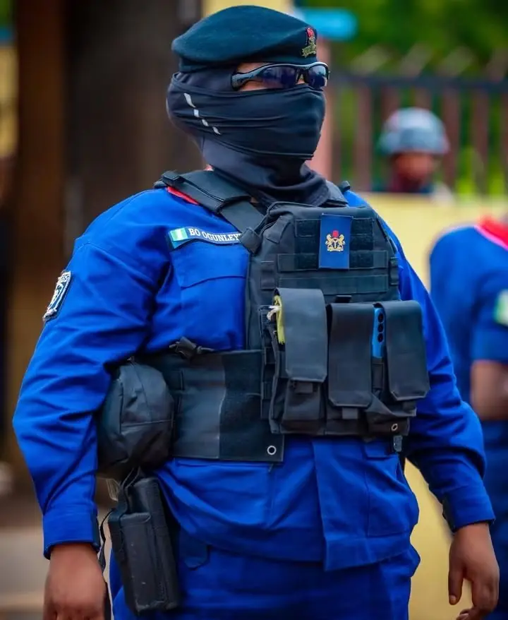 NSCDC Personnel - THEWILL NEWS MEDIA Masked security officer in a blue uniform with a tactical vest and protective eyewear.