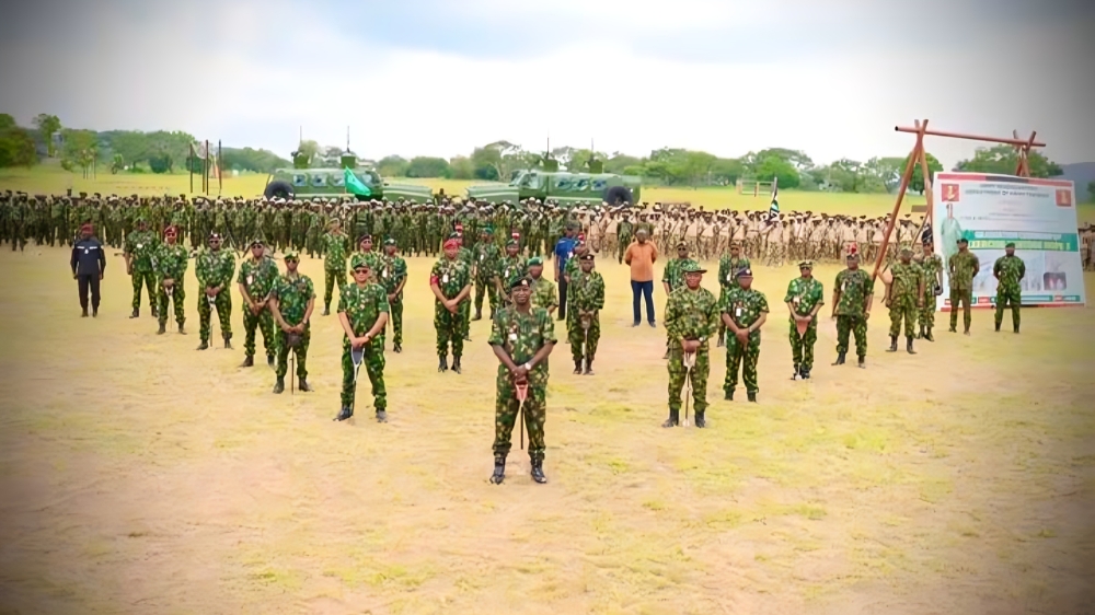 Newly trained Nigerian Army personnel - THEWILL NEWS MEDIA Soldiers in camouflage uniforms stand in rows on a dusty field during a training ceremony, with vehicles and a banner in the background.