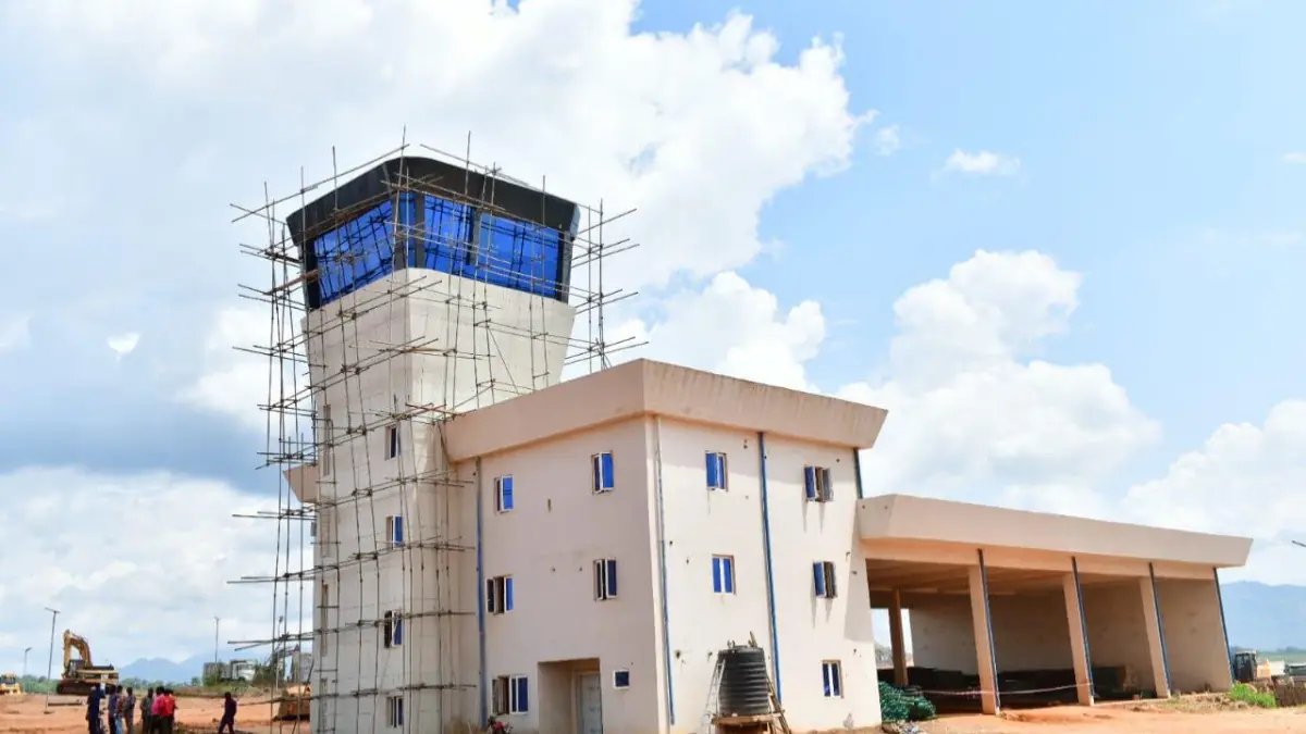 Obudu Cargo Airport - THEWILL NEWS MEDIA Construction site with a tall, scaffold-wrapped tower and a beige building with blue-framed windows against a bright sky.