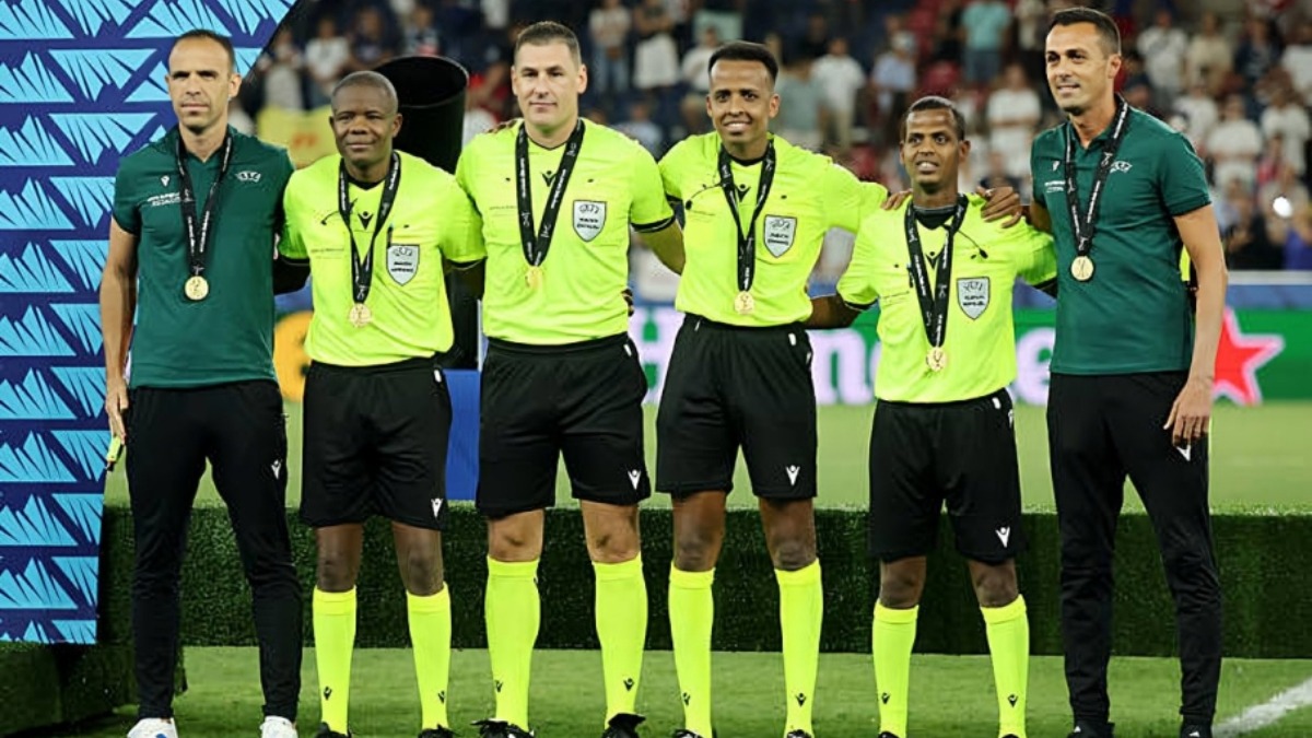 Omar Abdulkadir Artan with some officials - THEWILL NEWS MEDIA Five referees in neon yellow uniforms with medals pose on a soccer field. End officials wear green tops; a crowd watches in the background.