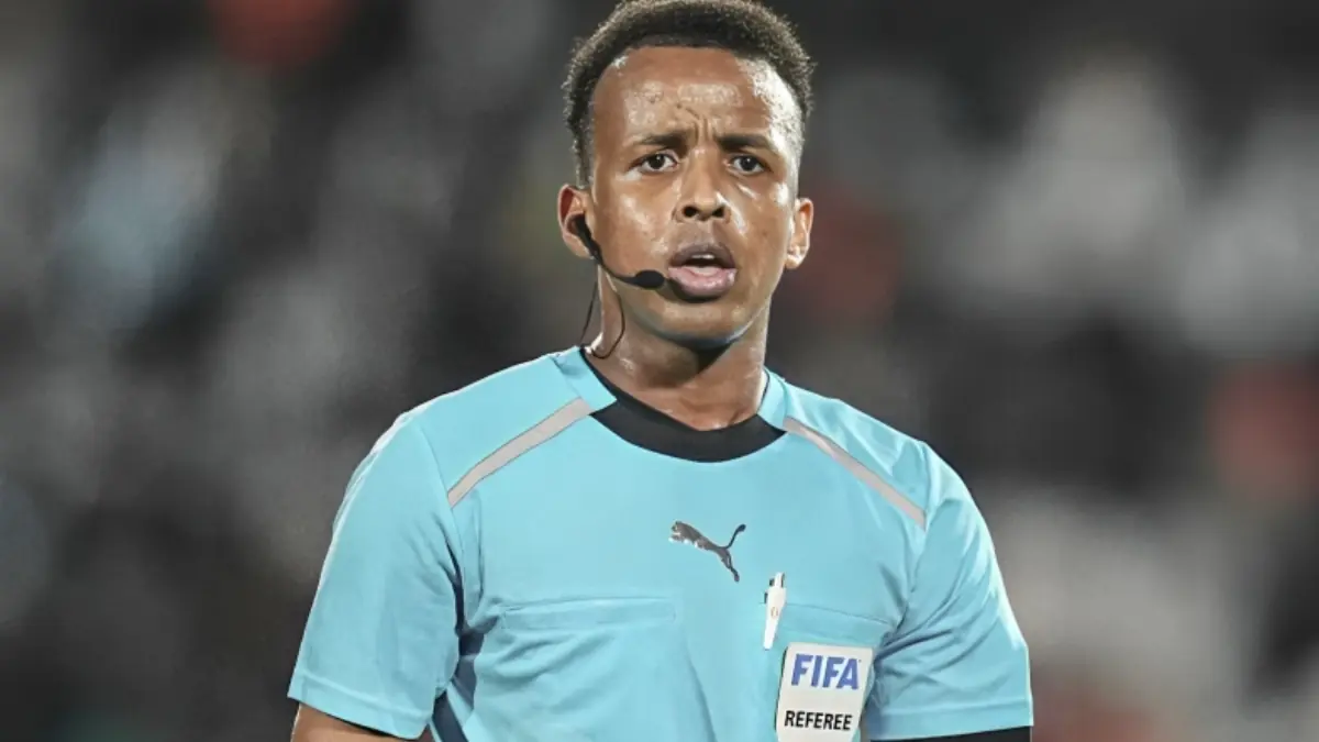 Omar Artan - THEWILL NEWS MEDIA Male soccer referee in a light blue shirt with a FIFA badge and headset, looking focused on the game.