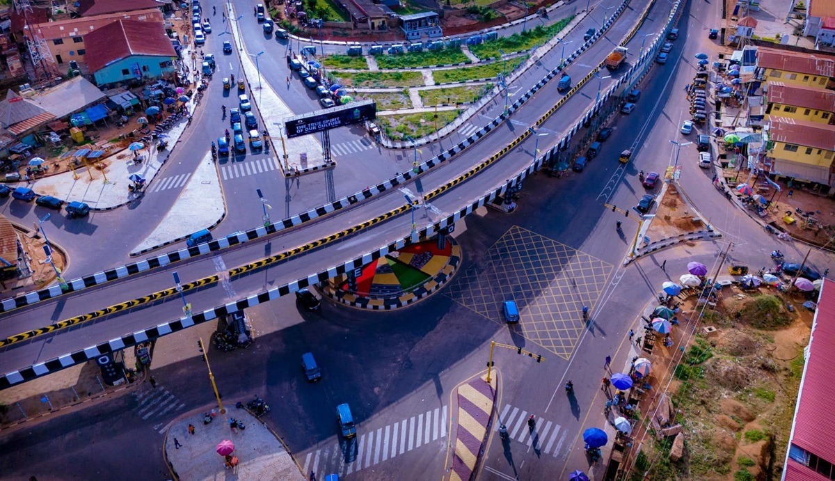 Osun state 2 - THEWILL NEWS MEDIA A busy elevated road interchange with a circular underpass, zebra crossings, and vendors with umbrellas along the sidewalks.