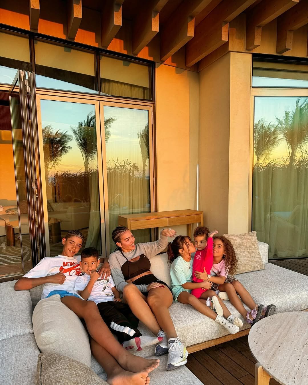 Para quem está sempre lá Feliz Dia da Mãe ❤️ - THEWILL NEWS MEDIA A smiling group of kids and a woman lounge on an outdoor sectional sofa on a sunny patio at sunset.