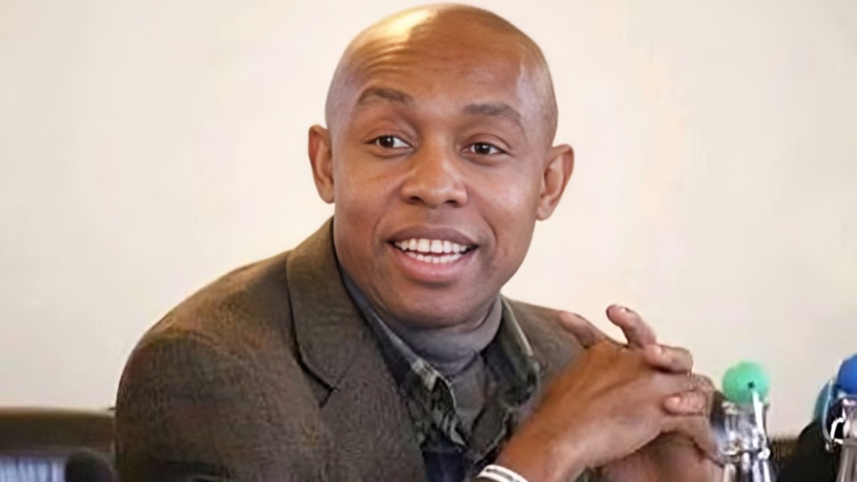 Professor Chidi Anselm Odinkalu - THEWILL NEWS MEDIA Smiling man in a brown blazer with folded hands at a conference table.