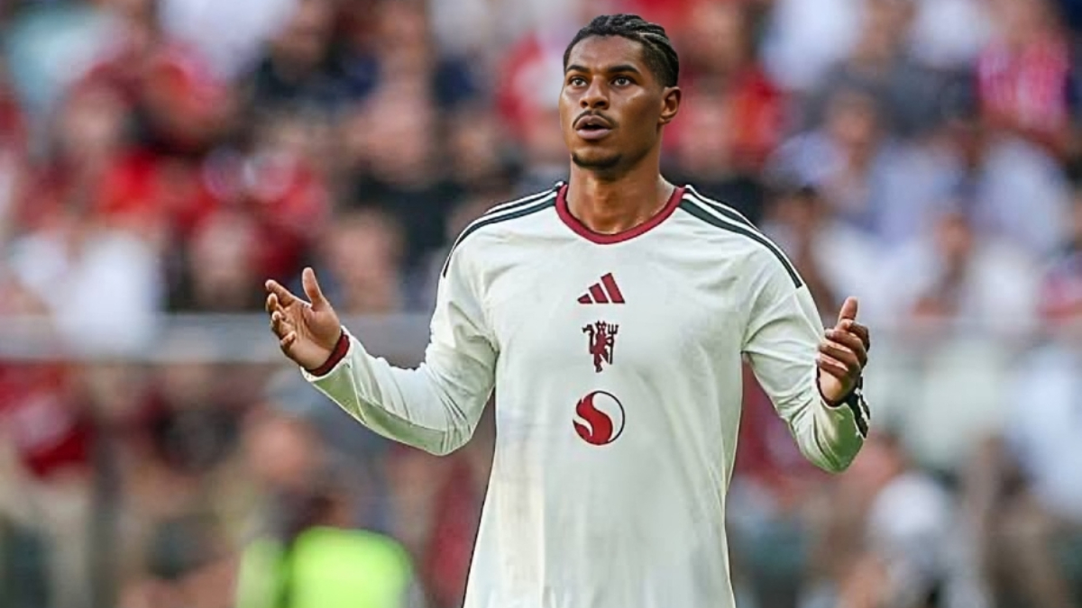 Rashford - THEWILL NEWS MEDIA Male footballer in a white jersey with red trim raises arms in celebration on a crowded stadium field, blurred fans in the background.