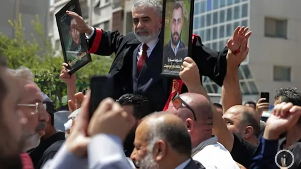 Relatives of victims and supporters gather outside a Damascus - THEWILL NEWS MEDIA Man in a suit lifts two framed portraits of men above a dense crowd at a protest.**BargeMoment**