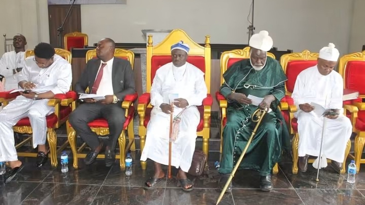 Religious leaders and participants at the Organisation of African Instituted Churches OAIC - THEWILL NEWS MEDIA Five men in ceremonial attire sit in a row on ornate gold-and-red chairs at a formal event, reading booklets or documents.