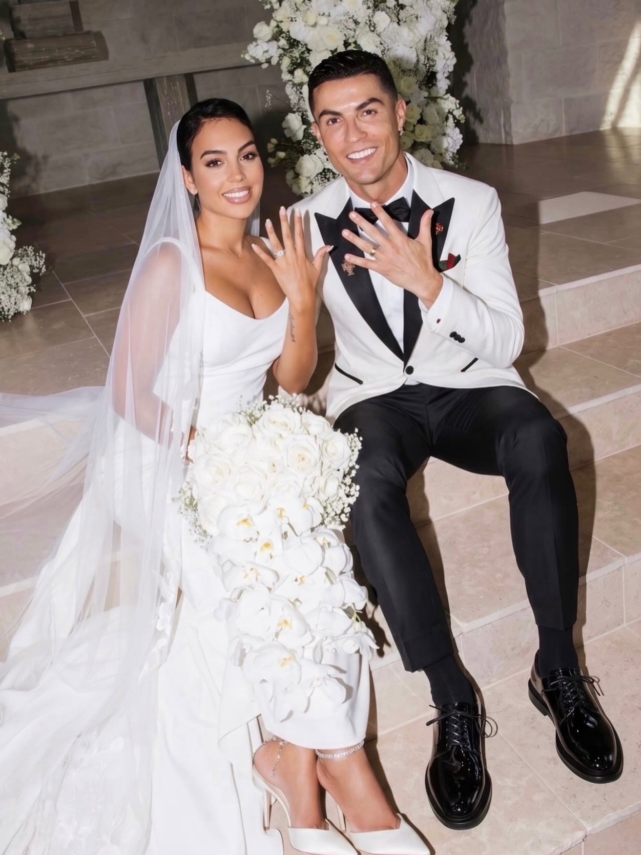 Ronaldo and Geogina - THEWILL NEWS MEDIA Bride and groom seated on steps, showing their wedding rings; she in a white gown with veil, he in a white tuxedo jacket and black bow tie.