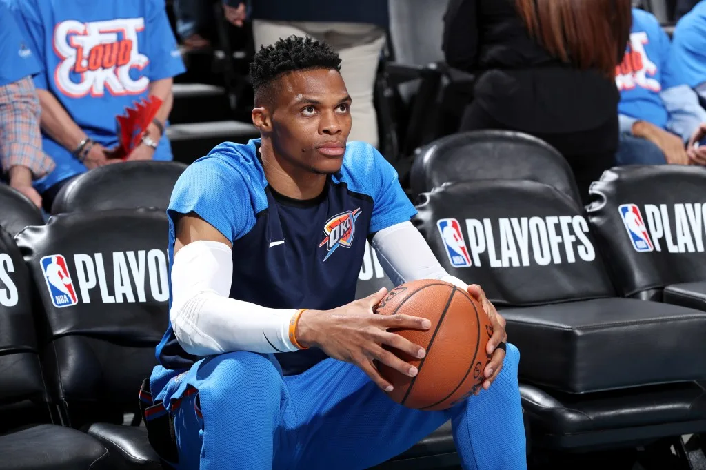 Russel - THEWILL NEWS MEDIA Basketball player in OKC blue uniform sits on a bench, holding a basketball during the playoffs.
